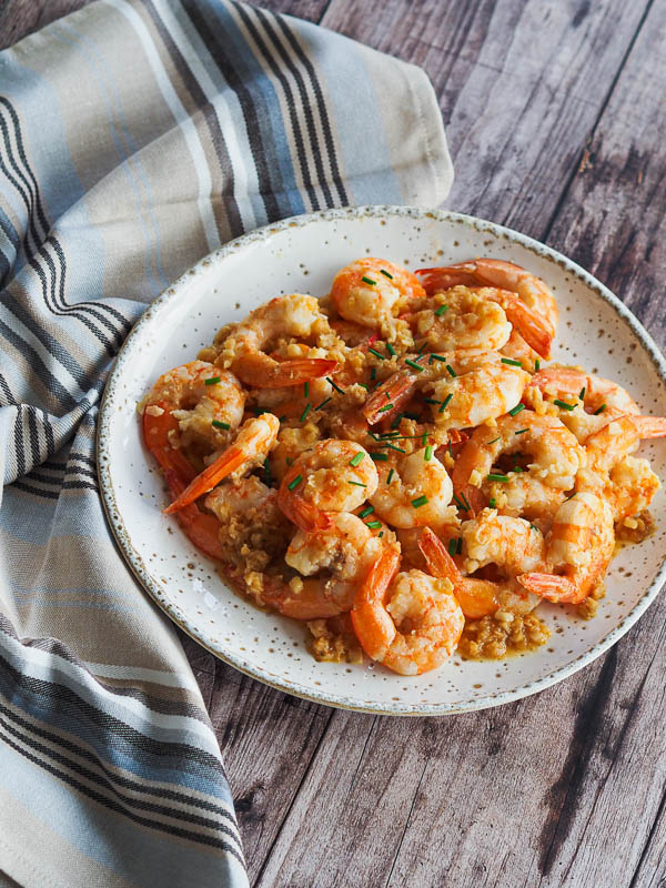 a colorful plate with shrimps cooke din garlic butter sauce and sprinkled with fresh herbs